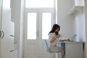 Woman in white kitchen at desk with laptop drinking coffee, Platinum Resumes, Kansas City, MO