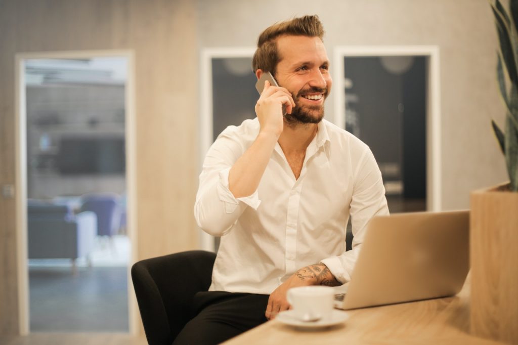 Man smiling on phone at laptop with coffee cup, Platinum Resumes, Kansas City, MO