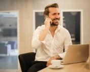 Man smiling on phone at laptop with coffee cup, Platinum Resumes, Kansas City, MO