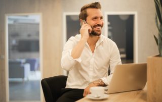 Man smiling on phone at laptop with coffee cup, Platinum Resumes, Kansas City, MO